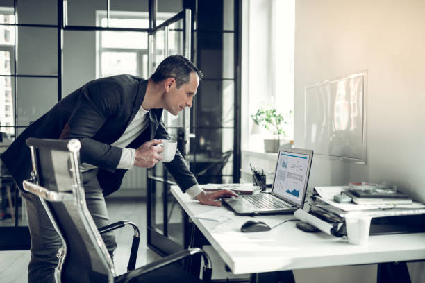 hombre maduro leyendo informe en el ordenador portátil mientras bebe café - manager marketing recruitment small business fotografías e imágenes de stock