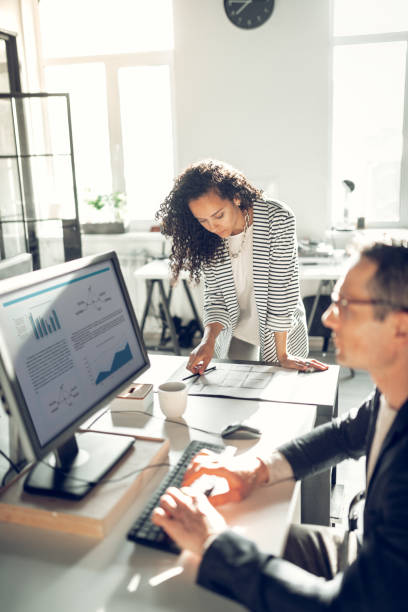 istock Curly secretary standing near her boss working on computer 1152229818