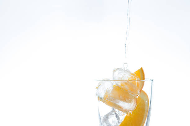 ice drink with orange and ice in the studio on a white background. a stream of water pours into the glass. - carbonic acid imagens e fotografias de stock