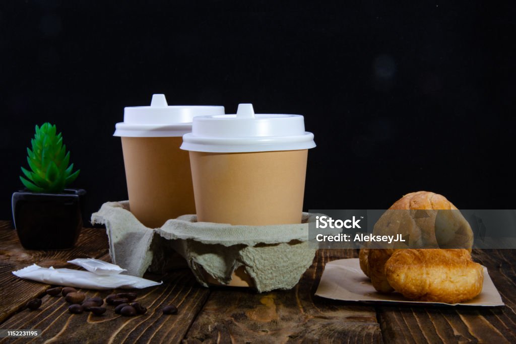 Paper cups of coffee, sugar in bags, donuts. Croissant. Wooden table. Black background. Horizontal Stock Photo