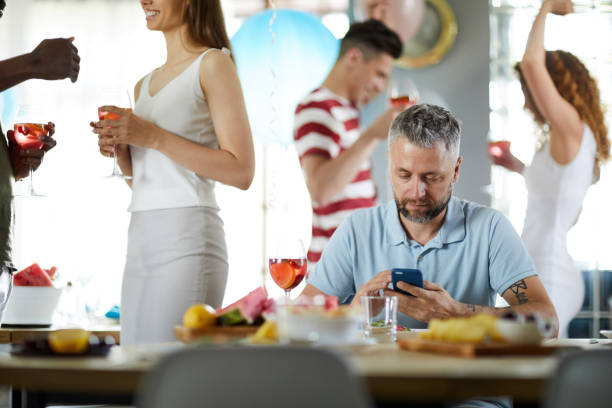 Bored Man at Party Portrait of bored mature man using smartphone at party, copy space exclusive dinner stock pictures, royalty-free photos & images