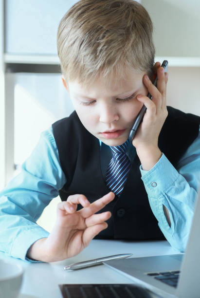 istock Smart little boy in suit working on computer, taking notes and speaking on the phone emotionally. 1152235899