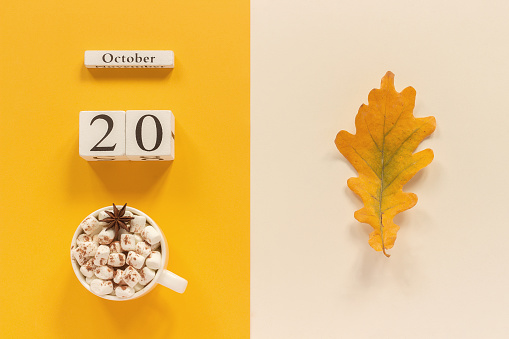 Autumn composition. Wooden calendar October 20 , cup of cocoa with marshmallows and yellow autumn leaves on yellow beige background. Top view Flat lay Mockup Concept Hello September.