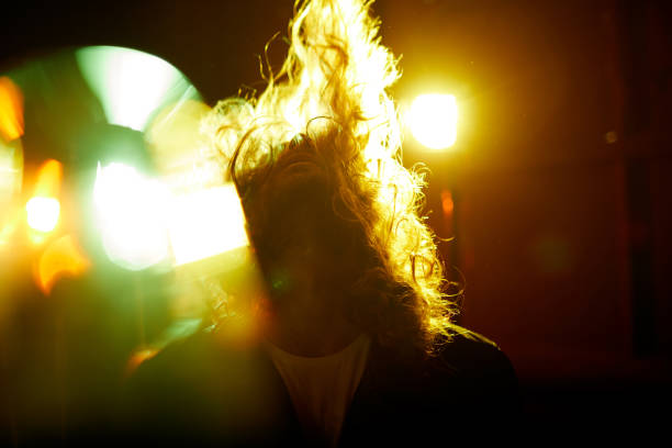 Energetic young male rock musician shaking hair while performing in disco lights at musical concert