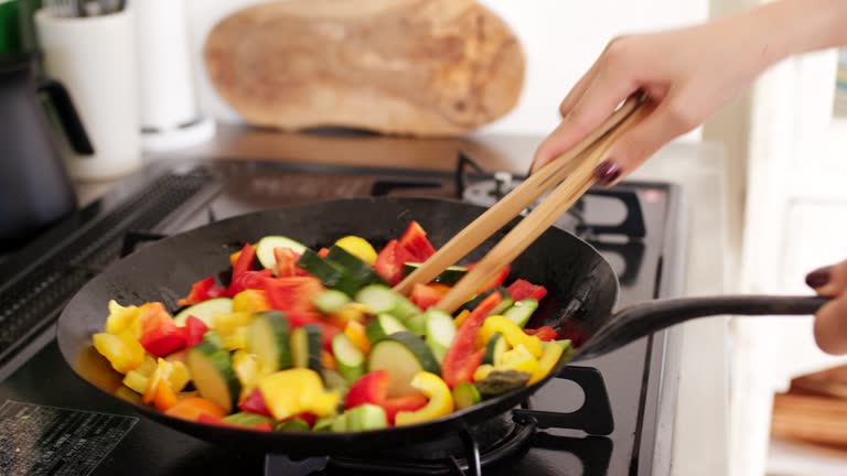 Close-up of a young woman cooking vegetables in a wok