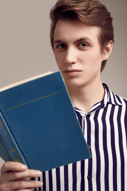 istock Young handsome man in striped shirt reading a book on gray background 1152249104