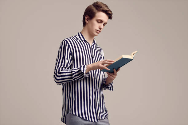 istock Young handsome man in striped shirt reading a book on gray background 1152249126