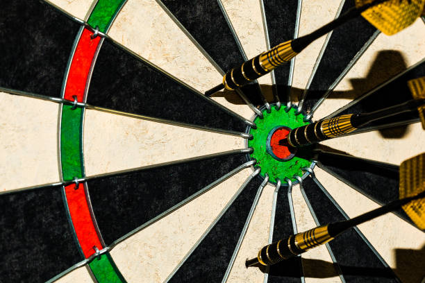 ein near macro schuss eines bullseye wurf eines stahlspitzes dart mit 2 anderen darts auch im spielfeld.  die farbe ist sehr lebendig in diesem schuss und es gibt viel platz für kopie auf der linken seite der dart-tipps. - dart bulls eye darts dartboard stock-fotos und bilder