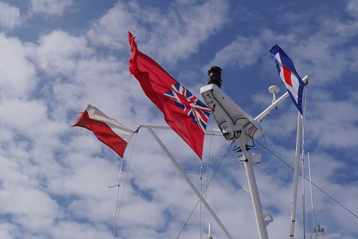 The 'red ensign' flag of the United Kingdom flying on the mast of a commercial ferry on a bright day with a little cloud cover