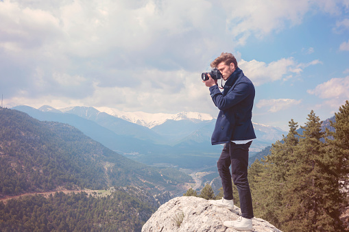 Young hiker man taking photos of mountains on top of mountain peak.
