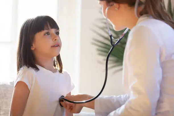 Pediatrician doctor in white uniform listening to lung and heart sound of little girl, child, patient with stethoscope, physician checkup at home or in hospital, children medical insurance care