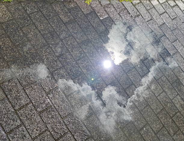 Reflection of the sky with sun and clouds in a puddle on the pavement