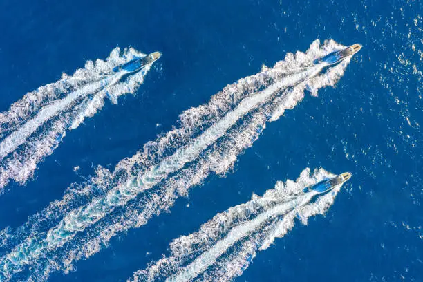 Three speed boats launch at high speed floats in the ocean, aerial top view