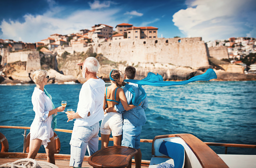 Closeup rear view of mid 60's couple enjoying a sailing cruise during  summer vacation at seaside. They are looking at a medieval fortress on the coastline.