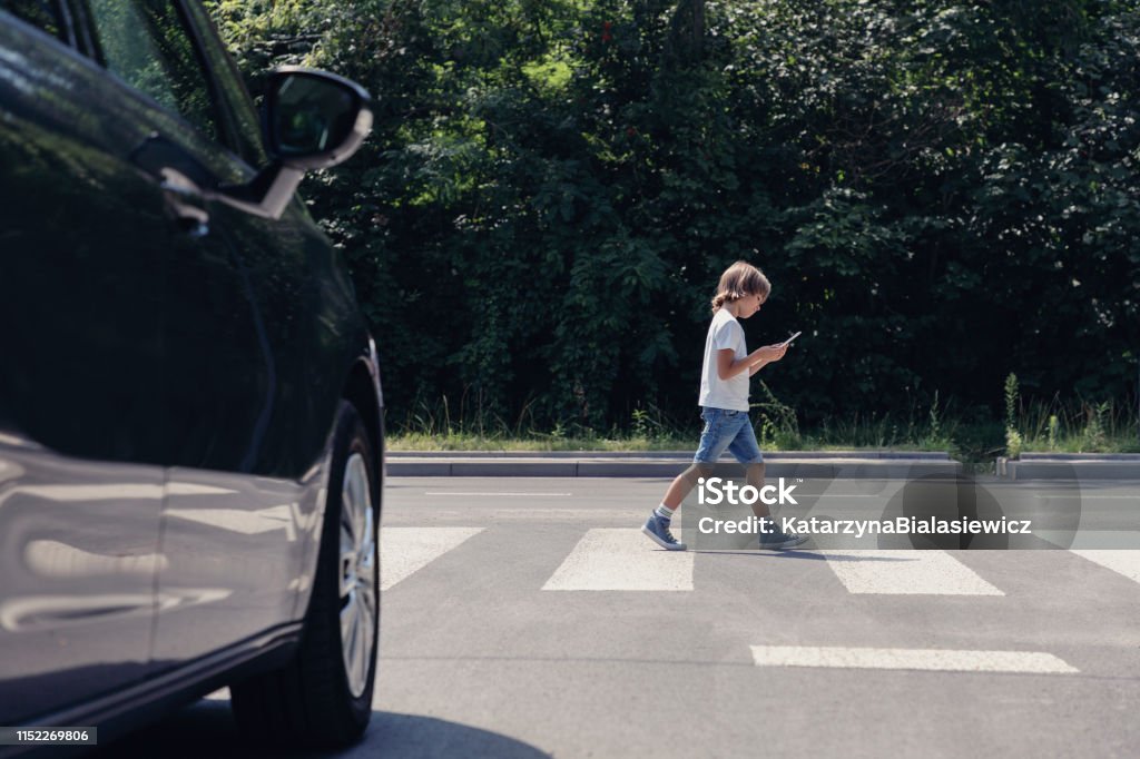 Bajo ángulo de coche en frente de cruce peatonal y caminar niño con teléfono inteligente - Foto de stock de Peatón libre de derechos
