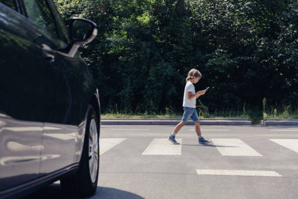 Low angle of car in front of pedestrian crossing and walking boy with smartphone Low angle of car in front of pedestrian crossing and walking boy with smartphone pedestrian stock pictures, royalty-free photos & images