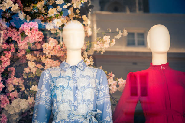 Horizontal color image depicting plastic mannequins wearing colorful floral-patterned womens blouses in a shop window. Behind the dummies is a beautiful fresh flower arrangement. We can see the reflections on the glass of the window. Room for copy space.