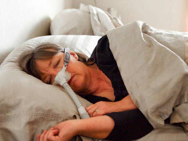 Middle Aged Woman With Sleep Apnea Asleep in a Bed Wearing a CPAP (Continuous positive airway pressure) machine to aid in her sleeping Middle Aged woman with sleep apnea Asleep in a Bed Wearing a CPAP (Continuous positive airway pressure) machine to aid in her sleeping sleep apnea photos stock pictures, royalty-free photos & images