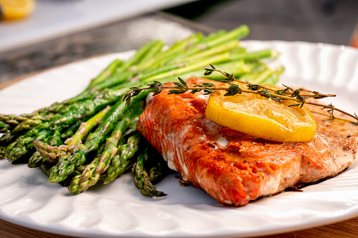 Beautiful sockeye salmon filet on a white plate with lemon slices and butter, with a side of asparagus part of a ketogenic or low carb diet.
