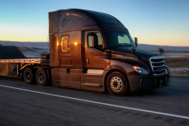 long haul semi truck rast down a four lane highway in a beautiful sunset - four lane highway stock-fotos und bilder