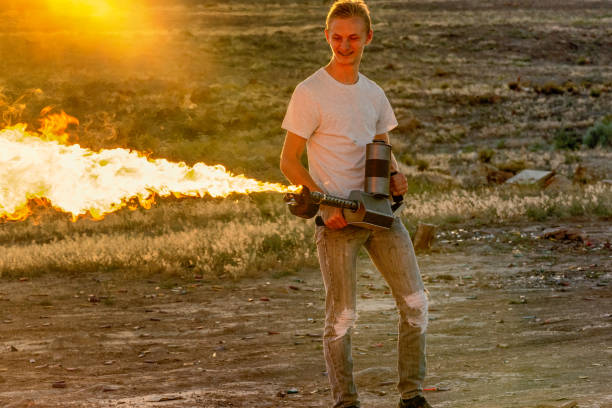 young man operating a flame thrower in the desert - flamethrower imagens e fotografias de stock