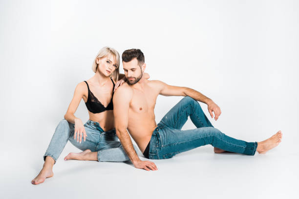 atractiva pareja joven en ropa interior y jeans sentados en gris - shirtless jeans women blond hair fotografías e imágenes de stock