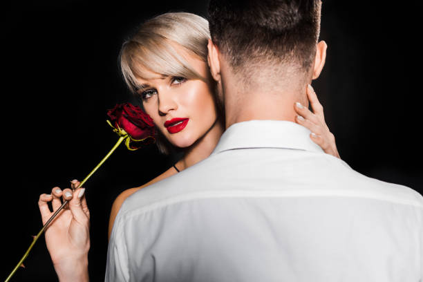istock sensual girlfriend holding red rose flower while hugging boyfriend, isolated on black 1152285415