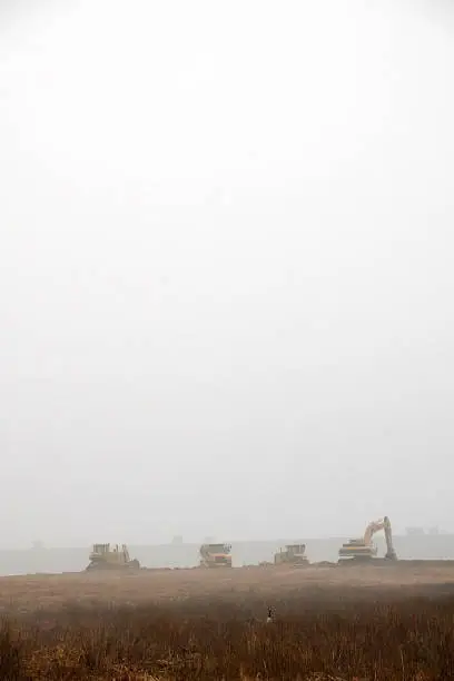 Construction equipment in a slight fog in the distance actively moving dirt. plenty of copy space
