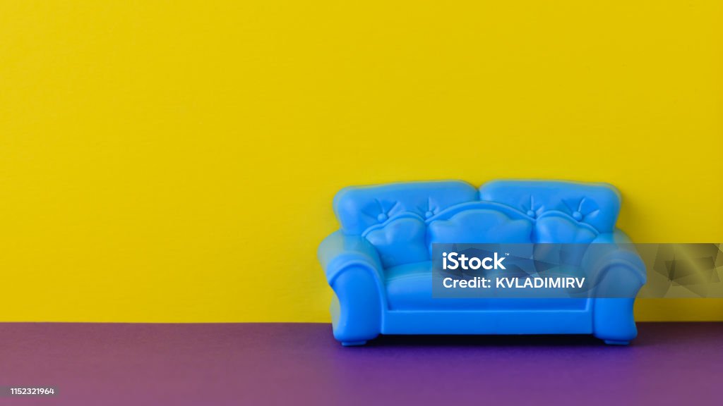 Beautiful blue sofa on the purple floor at the yellow wall. A sample of beautiful furniture for the house. Beautiful blue sofa on the purple floor at the yellow wall. A sample of beautiful furniture for the house. Minimalist. Backgrounds Stock Photo