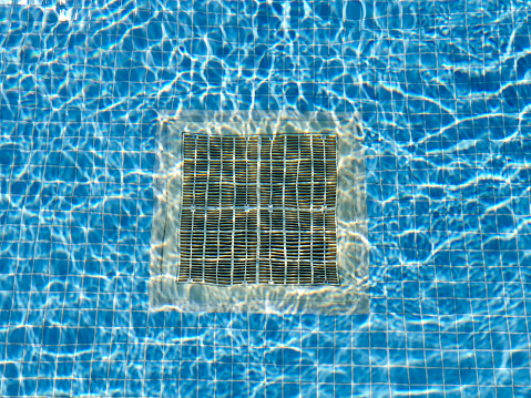Pulsating blue pool water with reflections of the sun.Drain grate for water at the bottom of the pool