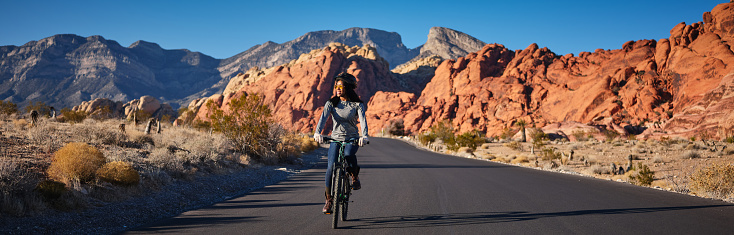 fit african american woman riding bicycle on road in red rock canyon park