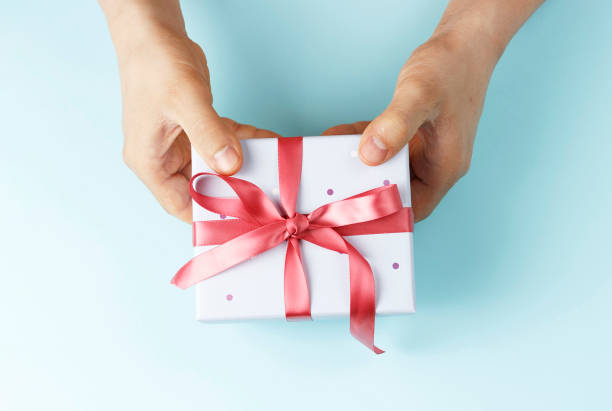 istock Male hands holding gift box with ribbon on blue background, top view 1152334905