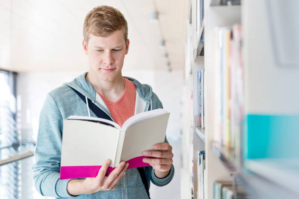 istock Serious young man reading book at university library 1152334959