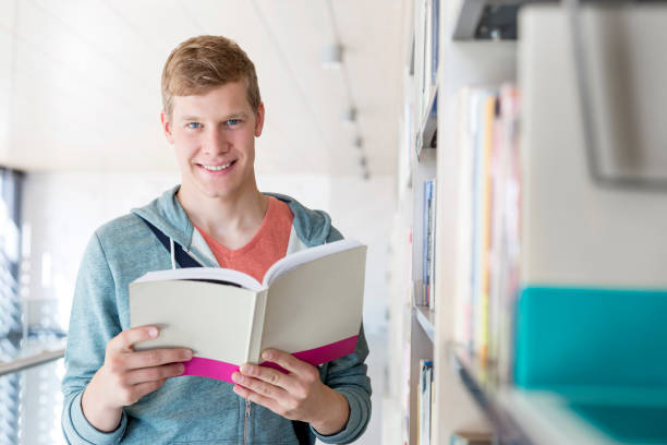 istock Portrait of smiling student reading book at library in university 1152335825