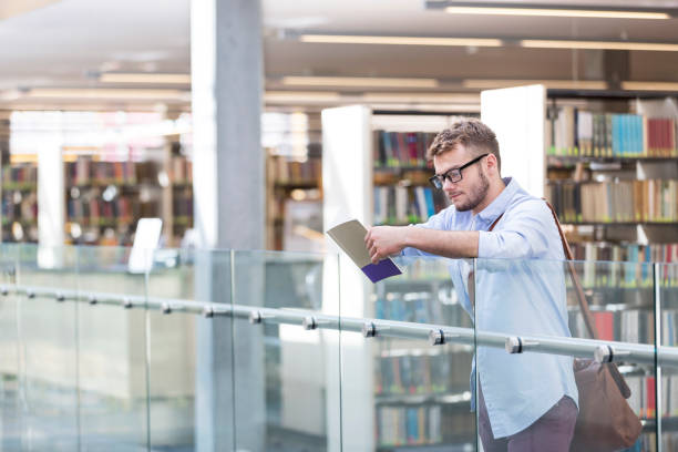 istock Young man reading book at railing against in library university 1152335986