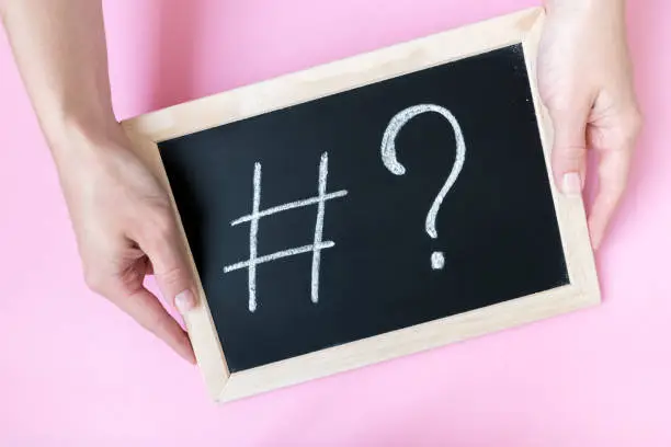 Photo of Female hands holding a blackboard with a chalk hashtag and a question mark written on it.