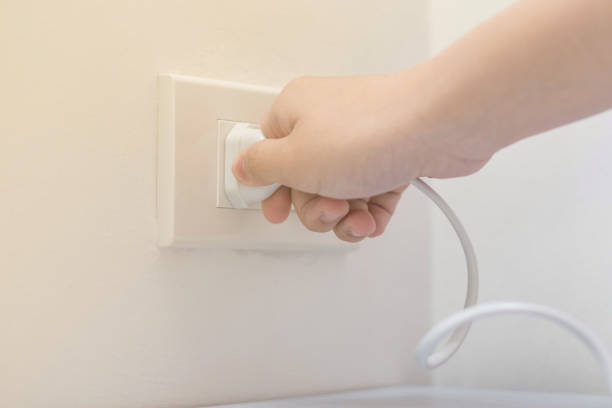 enchufe conector eléctrico en fondo de pared blanca con la mano haciendo el cable de desenchufar. ahorro energético de energía para el concepto de día mundial del medio ambiente. - electric plug outlet pulling electricity fotografías e imágenes de stock