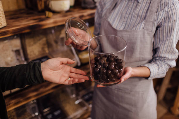 Shop assistant holding glass jar with healthy chocolate balls in organic store. stock photo