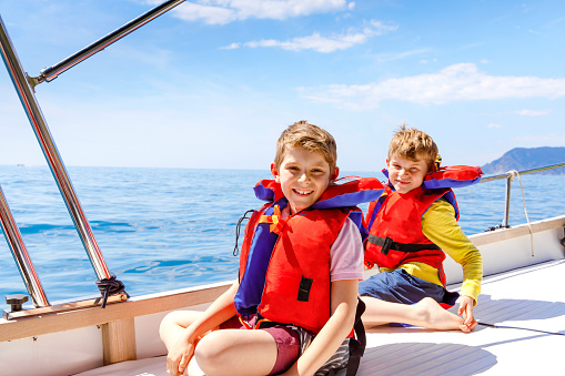 Two little kid boys, best friends enjoying sailing boat trip. Family vacations on ocean or sea on sunny day. Children smiling. Brothers, schoolchildren, siblings having fun on yacht