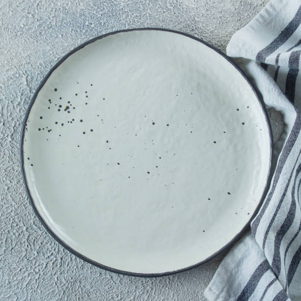 istock Empty ceramic plate and kitchen striped towel on light stone concrete table background. Copy space. Menu Recipe Concept. Top view. Flat lay 1152348365
