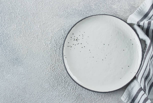istock Empty ceramic plate and kitchen striped towel on light stone concrete table background. Copy space. Menu Recipe Concept. Top view. Flat lay 1152348400