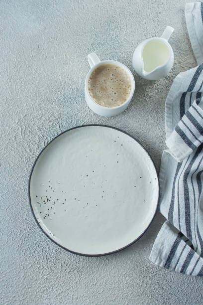 istock Empty ceramic plate, cup of coffee and kitchen striped towel on light stone concrete table background. Copy space. Menu Recipe Concept. Top view. Flat lay 1152348424
