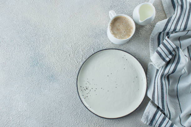 istock Empty ceramic plate, cup of coffee and kitchen striped towel on light stone concrete table background. Copy space. Menu Recipe Concept. Top view. Flat lay 1152348427