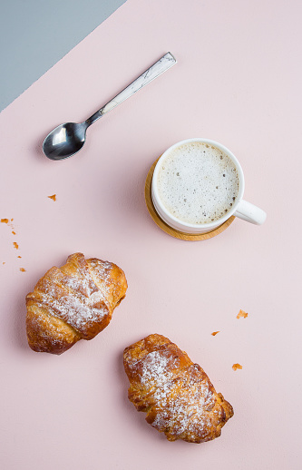 Two fresh croissants in a paper bag and cup of coffee on a two-color background, top view, copy space, flat lay
