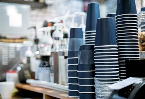 Close-up stack of upside down disposable cups. Interior of illuminated coffee shop. They are arranged on counter.