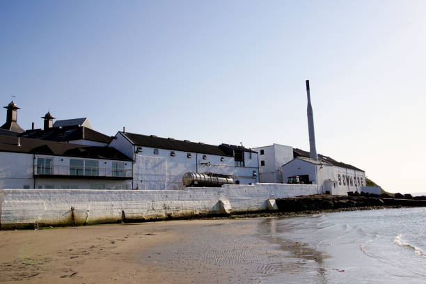 Bowmore, Islay, Scotland - May 01 2017: Bowmore Whisky Distillery Bowmore, Islay, Scotland - May 01 2017: The Bowmore Whisky Distillery seen from the beach of Loch Indaal in Bowmore bowmore whisky stock pictures, royalty-free photos & images