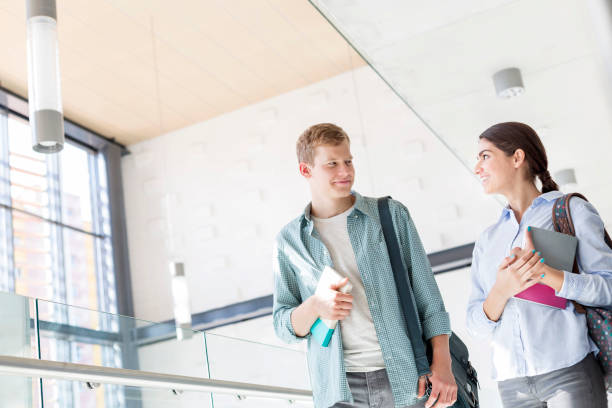 istock Smiling students with books talking while walking in corridor at university 1152356478