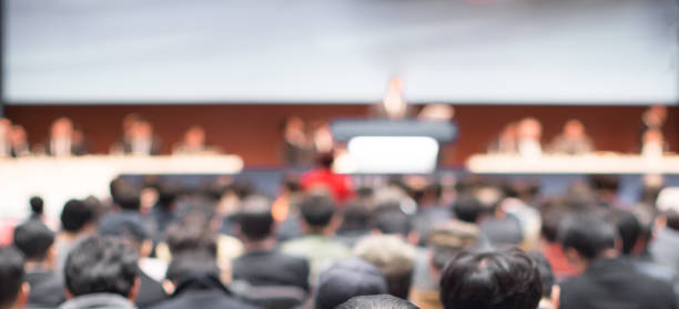 Blurred conference with panel speakers on stage during debate. Presenters at corporate seminar talking to audience.  Defocused business leadership CEO lecture. Executive board of directors. stock photo