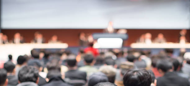 conferência borrada com os altofalantes do painel no estágio durante o debate. apresentadores no seminário corporativo conversando com o público.  palestra de ceo de liderança de negócios defocused. diretoria executiva. - accionista - fotografias e filmes do acervo