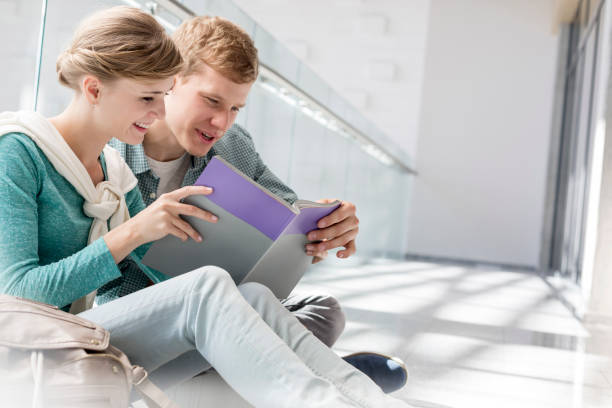 istock Smiling friends reading book while sitting on corridor at university campus 1152367905